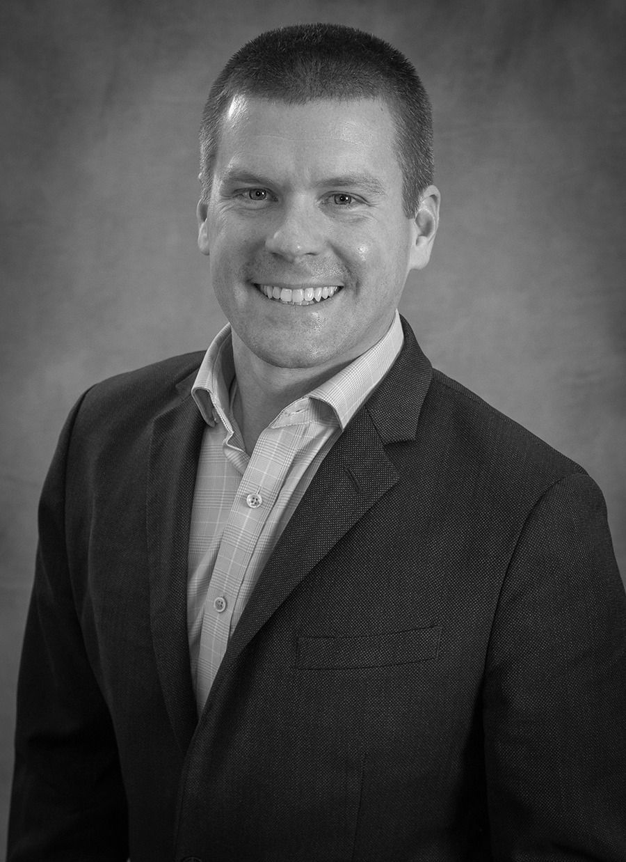 Smiling man in a blazer and collared shirt posed against a plain studio backdrop
