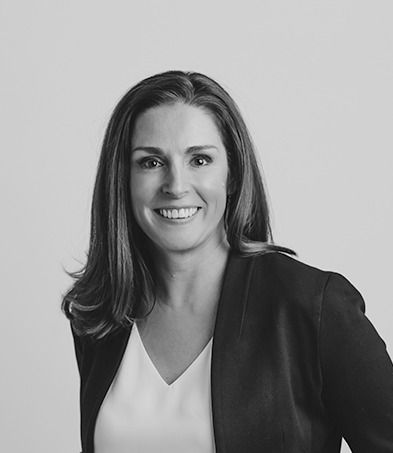 Smiling person in a black blazer and white top against a plain gray background