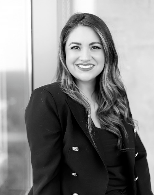 Woman smiling in a black blazer against a light wall.
