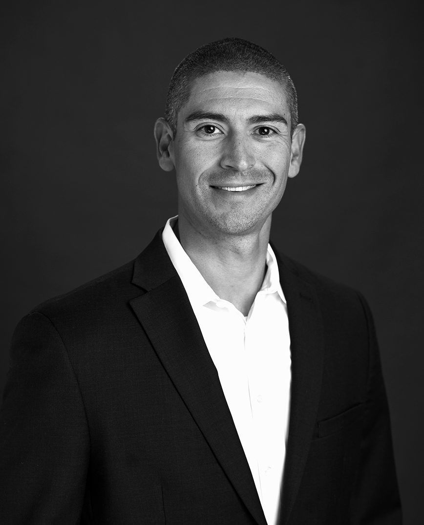Smiling person in a dark suit and white shirt against a black background.