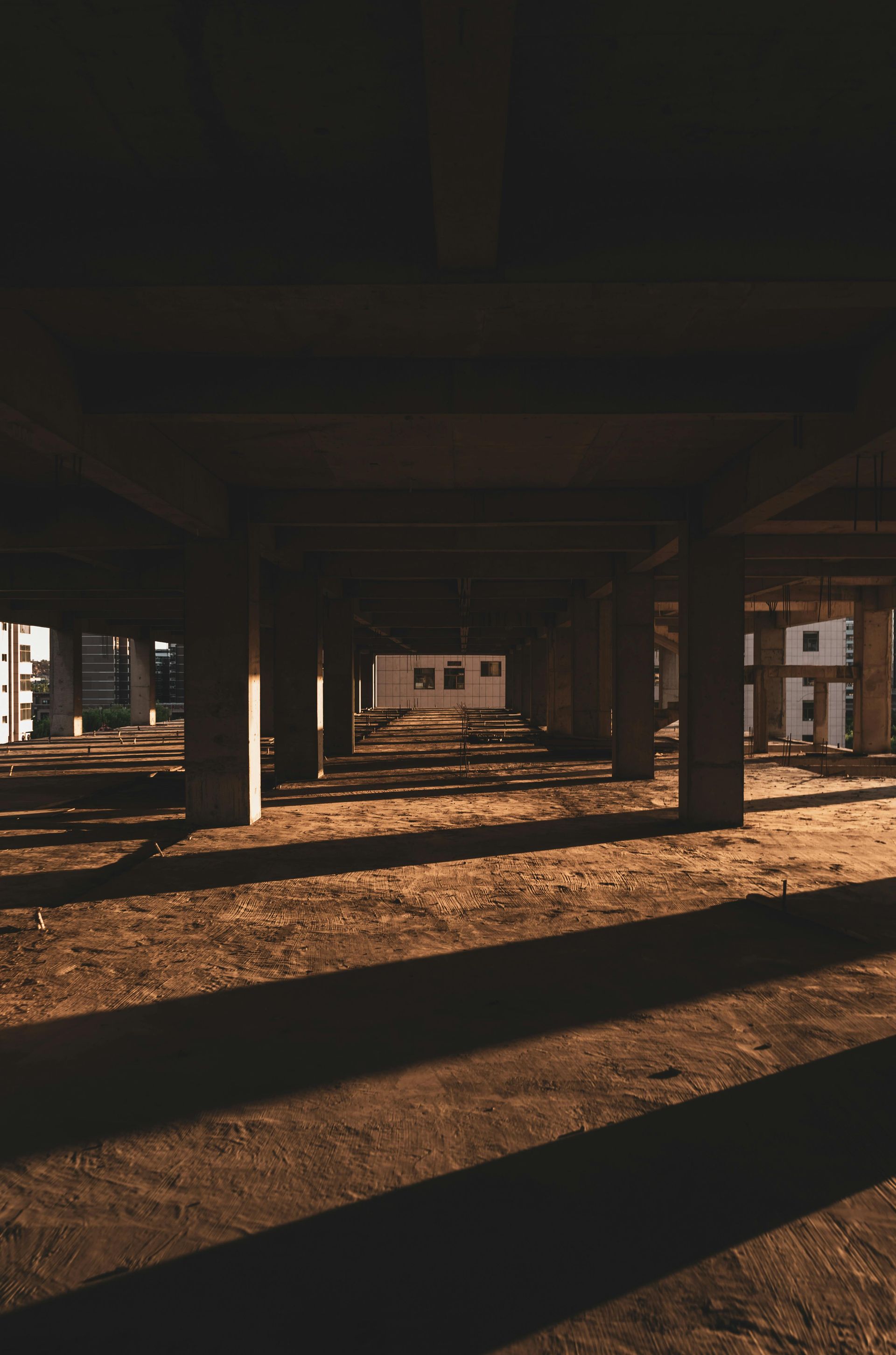 Sunlit concrete pillars under an elevated structure, casting long shadows across a dusty ground