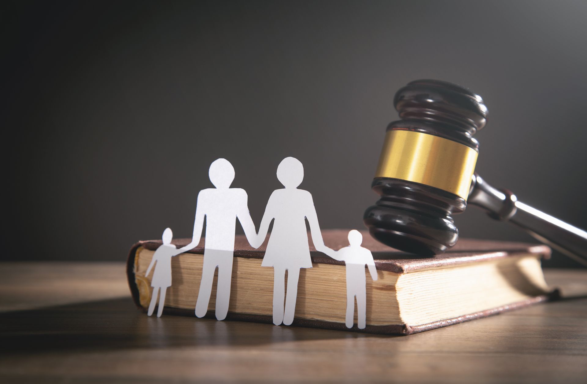 Paper cutout family on a law book with a judge’s gavel symbolizing family legal matters. Paper cutout family on a law book with a judge’s gavel symbolizing family legal matters.