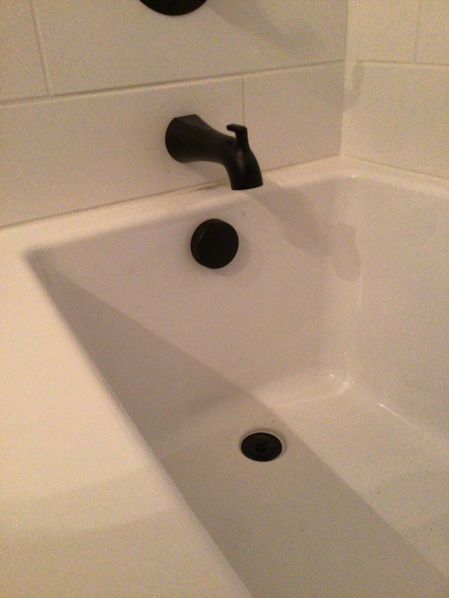 White bathtub with black faucet and drain against tiled bathroom wall.