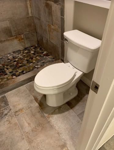 Small bathroom with a white toilet, stone tile floor, and walk-in shower with pebble floor.