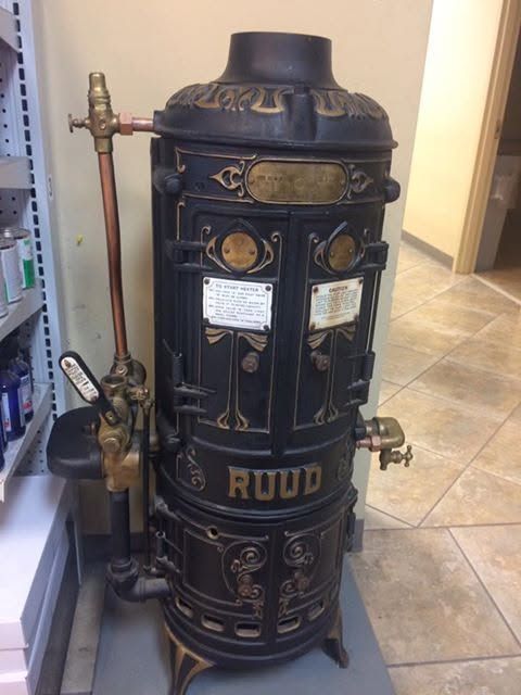 Tall black vintage RUUD furnace with brass details in an indoor hallway