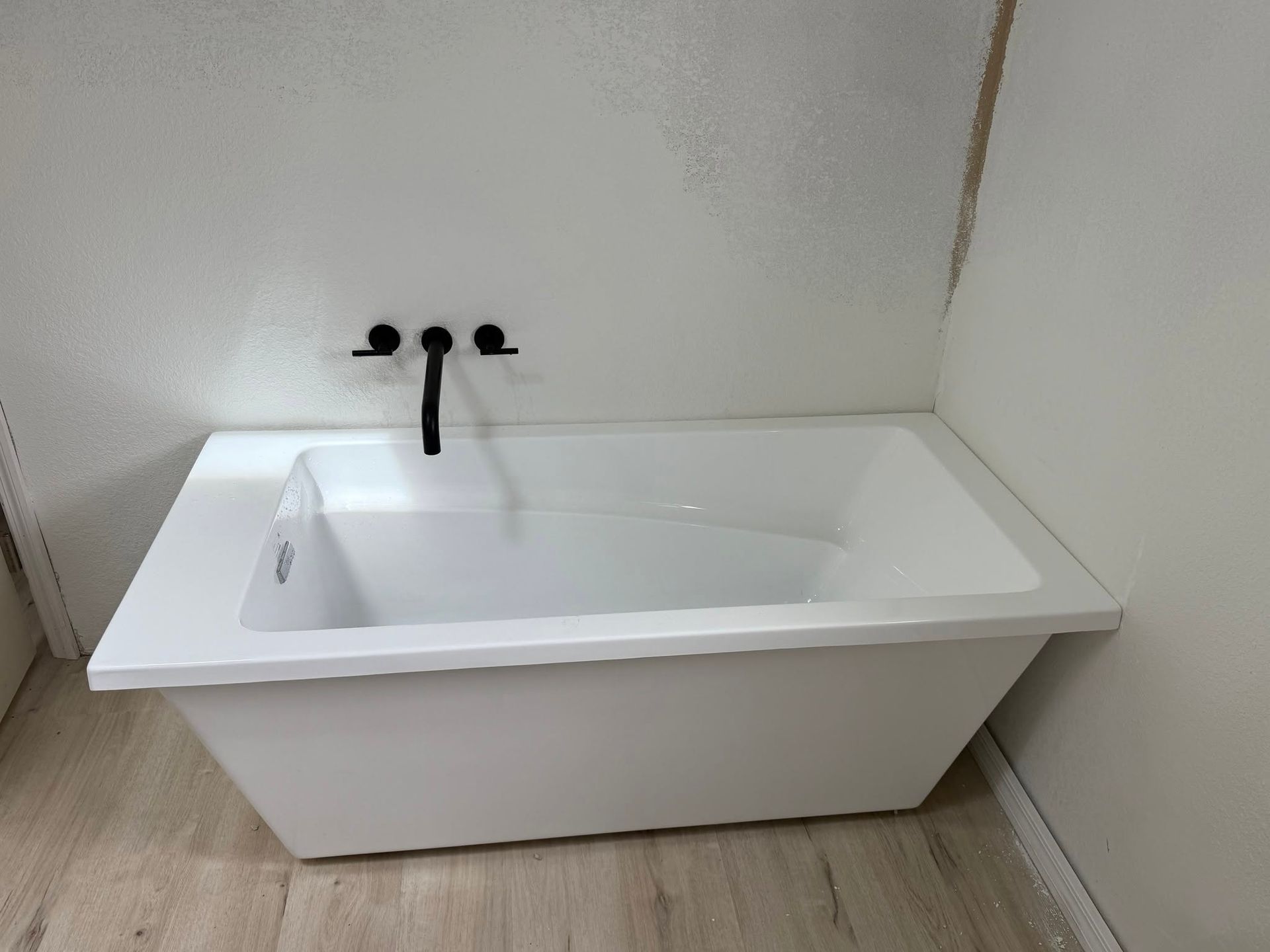White bathroom sink with black faucet against a plain wall