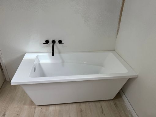 White bathtub with black faucet set against a plain light-colored wall.