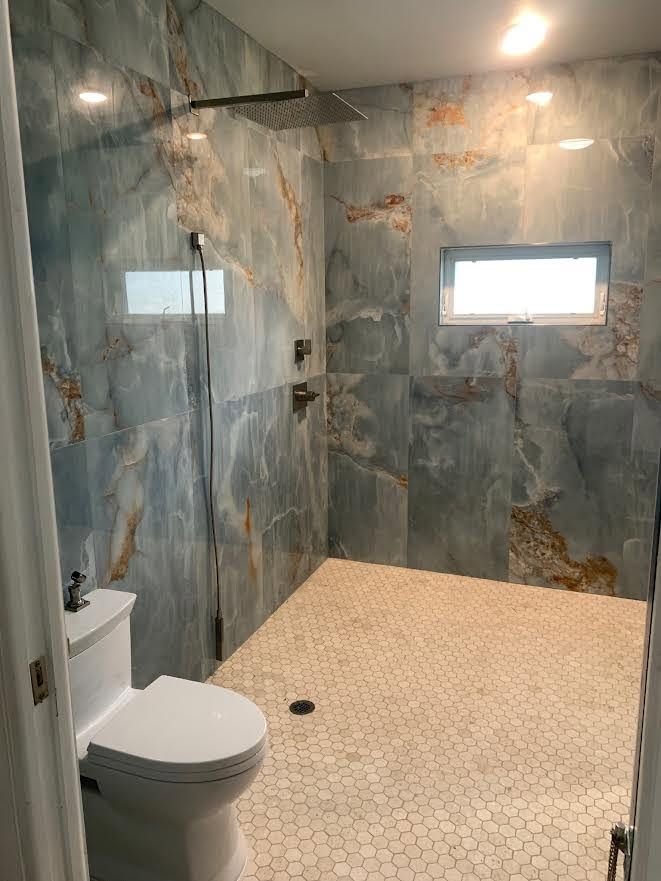 Stone-tiled bathroom with toilet, walk-in shower, and small window.