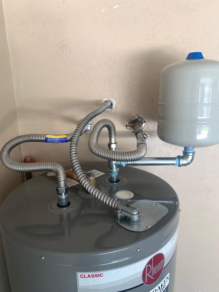 Water heater with coiled flexible hoses and a small white expansion tank against a beige wall