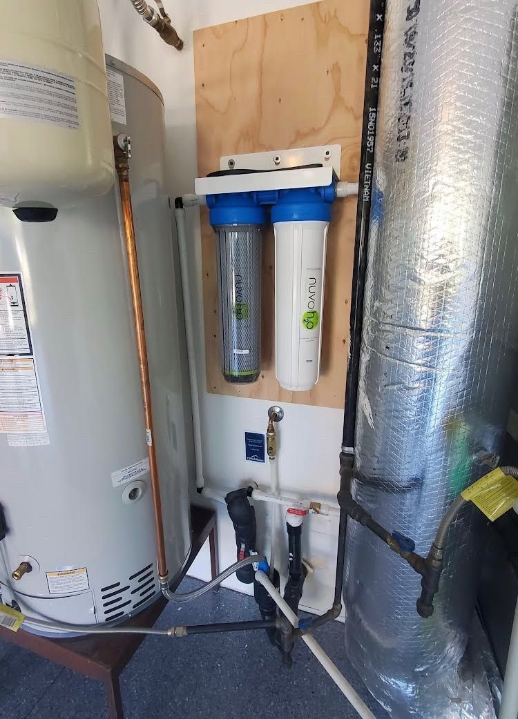 Water heater and water filter setup in a utility closet, with pipes, tanks, and insulation panels.