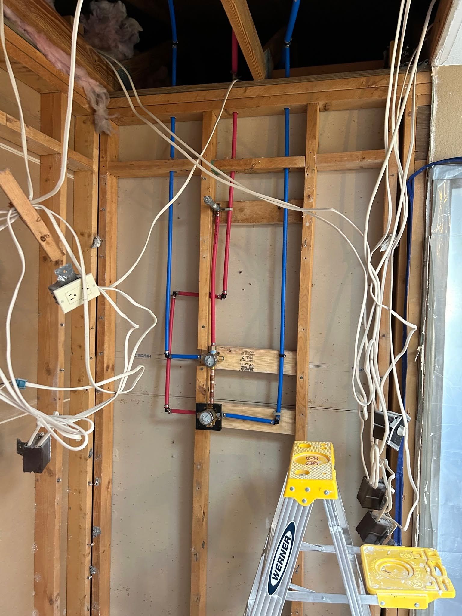 Unfinished wall framing with exposed wiring, ladder, and electrical boxes in a construction area