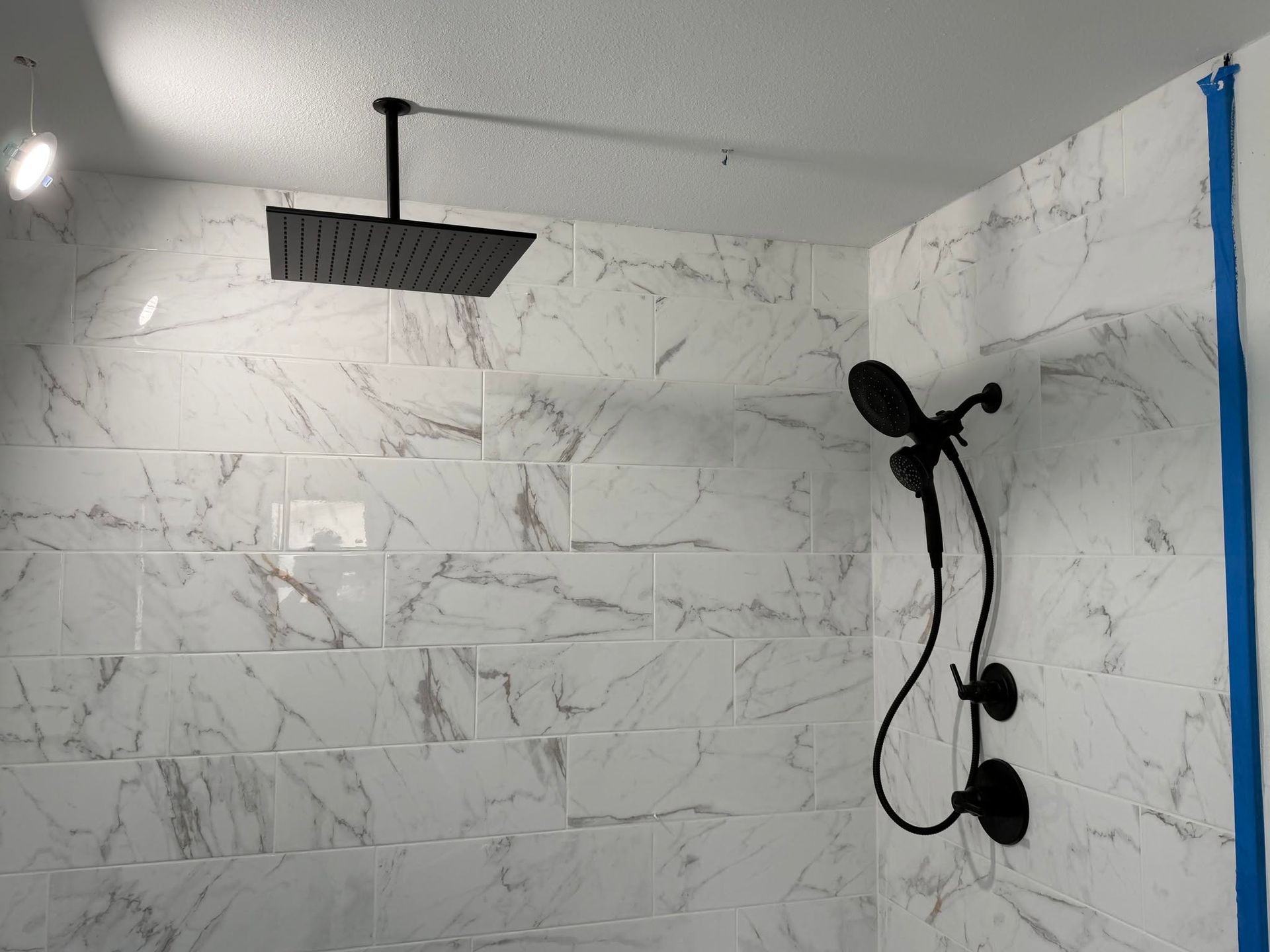 Modern bathroom shower with white marble-look tile, black fixtures, and ceiling rain shower head