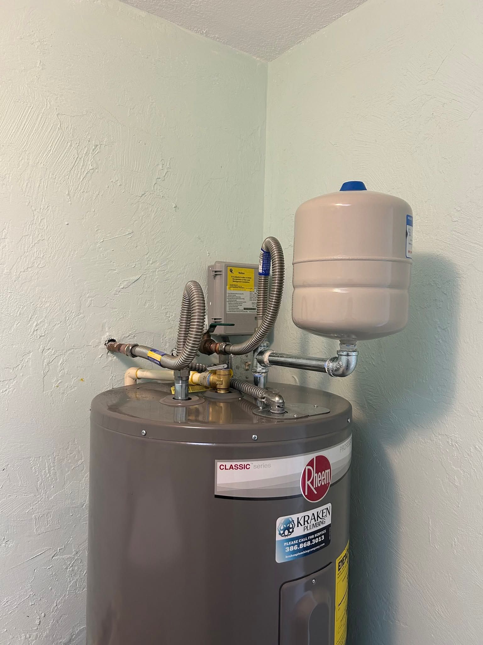 Water heater with plumbing and expansion tank in a corner utility room.