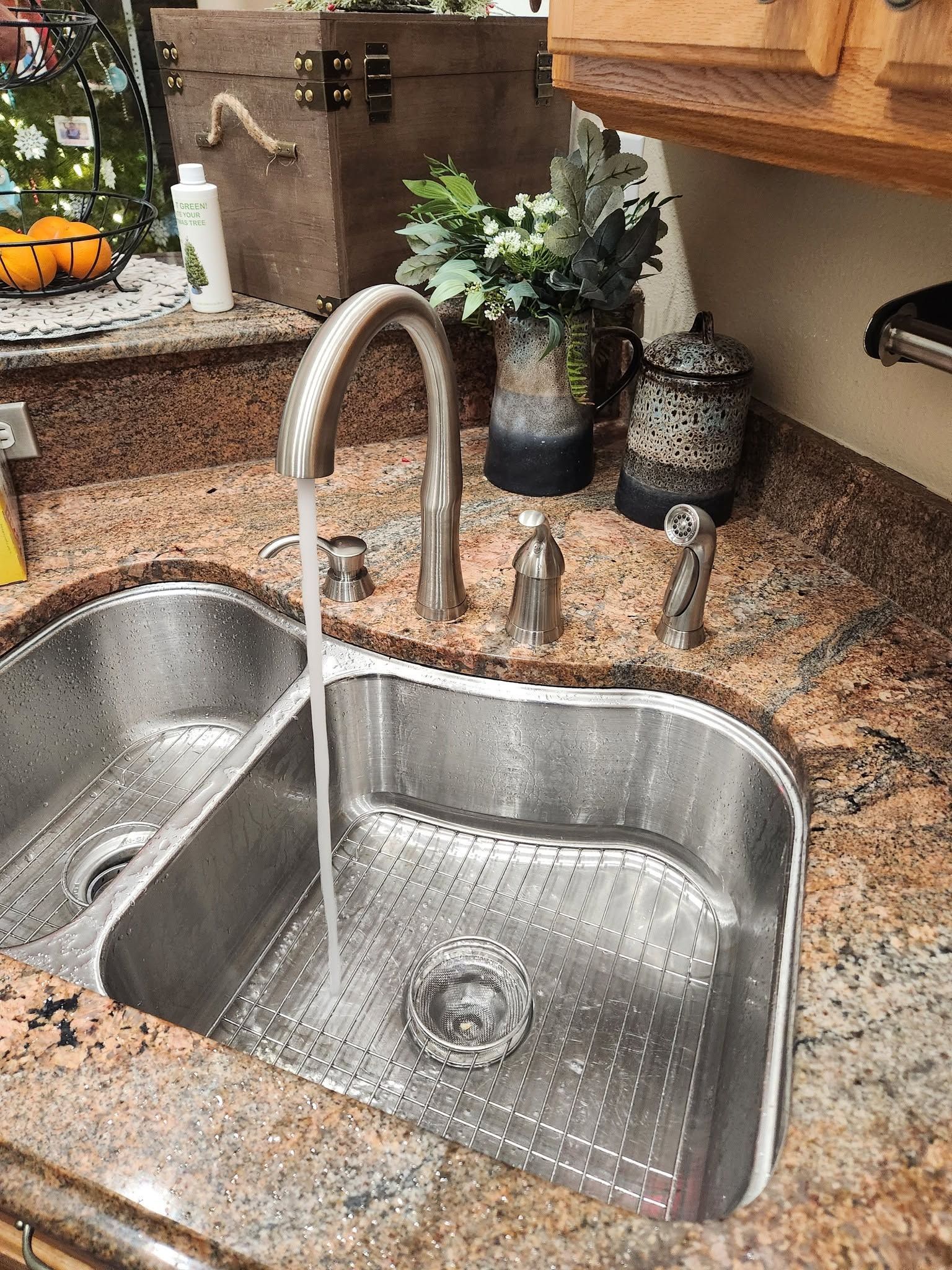 Stainless steel kitchen sink with running water, granite countertop, and soap dispensers beside a potted plant