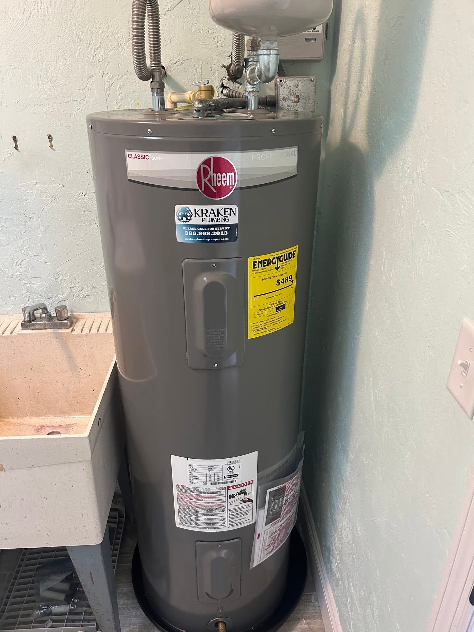 Gray water heater in a utility closet with warning labels and plumbing pipes on top.