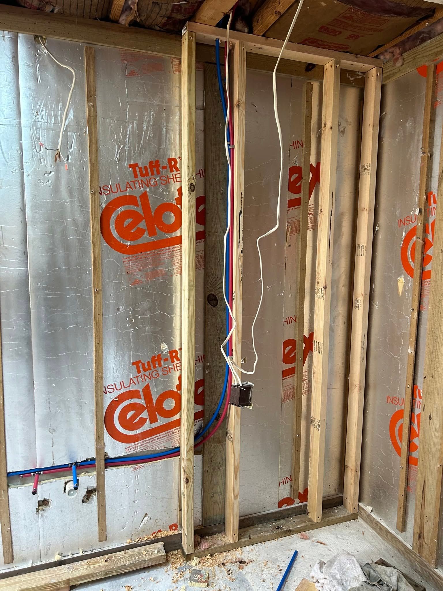Unfinished bathroom framing with insulation, exposed studs, and plumbing lines inside a small corner space