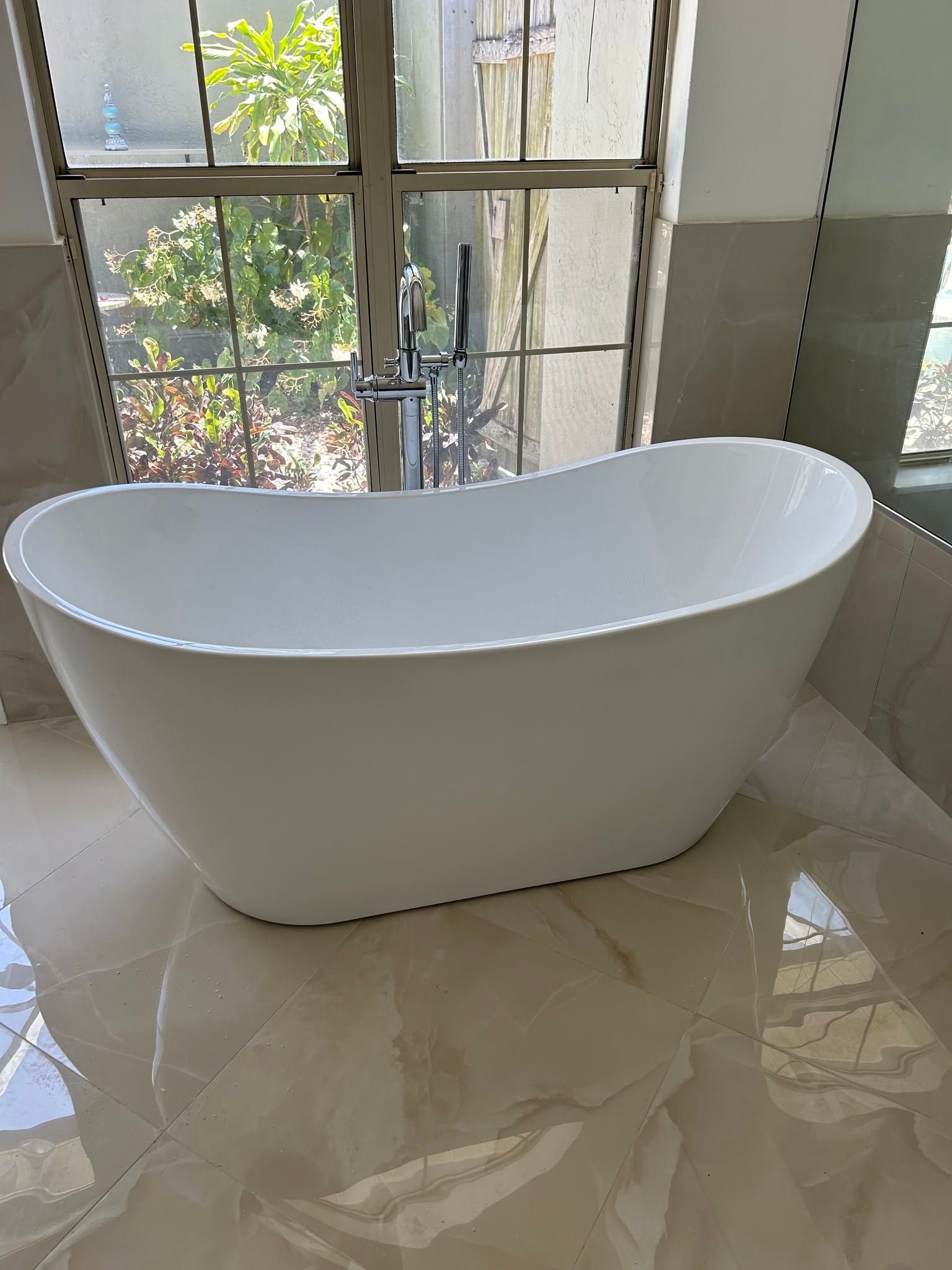 White freestanding bathtub by a window in a tiled bathroom
