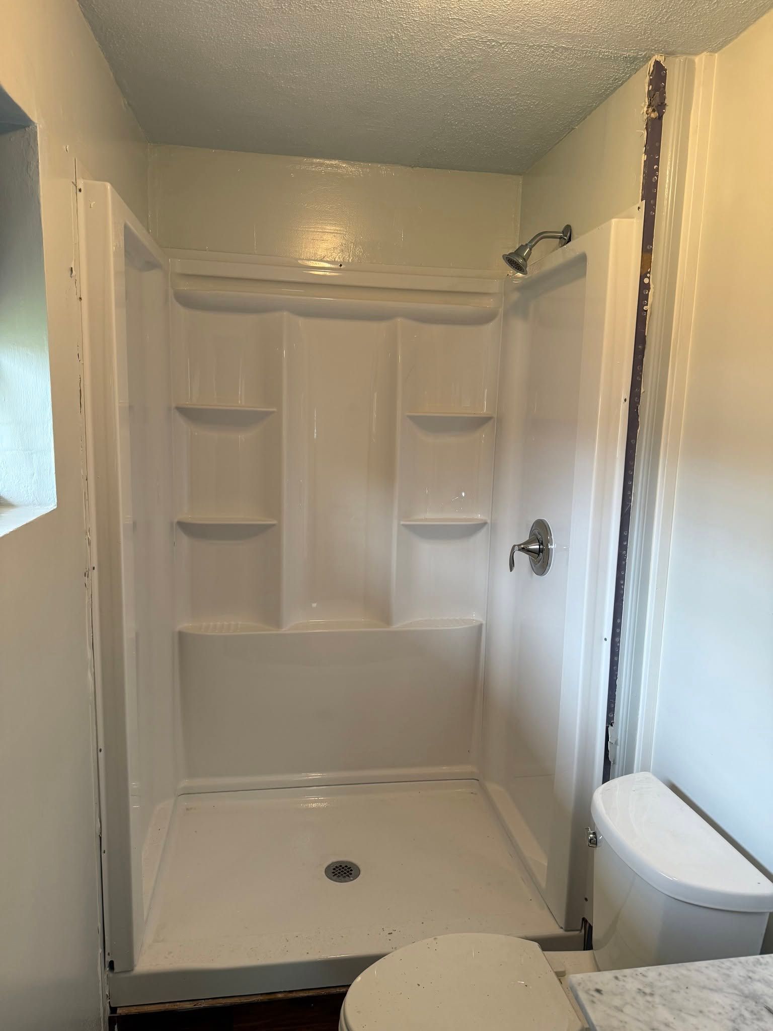Empty white shower stall with built-in shelves and a toilet beside it in a small bathroom