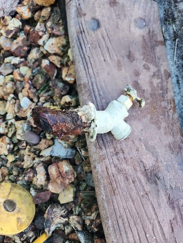 Small white figurine or toy lying on gravel beside a weathered wooden plank