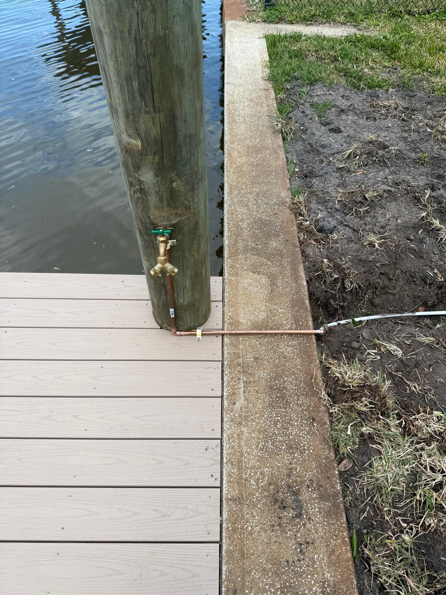 Dock beside water with a hose bib on a wooden post and a gravel path nearby