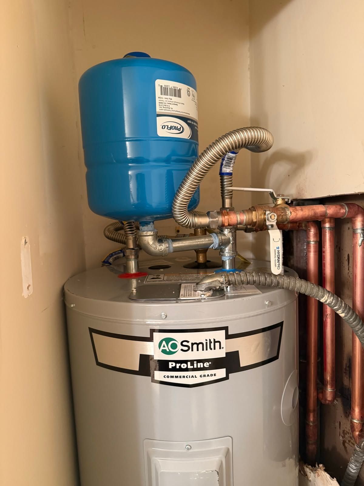 A blue expansion tank and gray A. O. Smith water heater in a utility closet, connected by copper pipes.