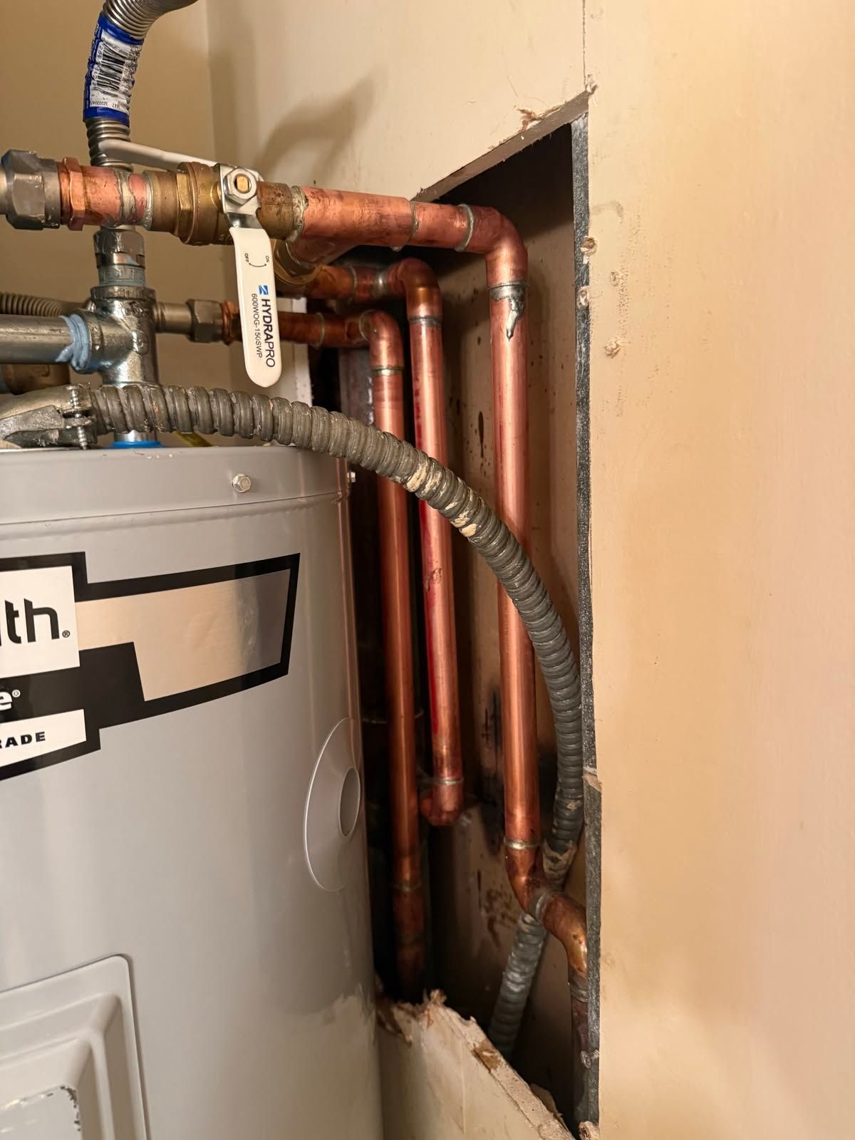 Water heater plumbing with copper pipes and valves in a wall opening inside a utility closet