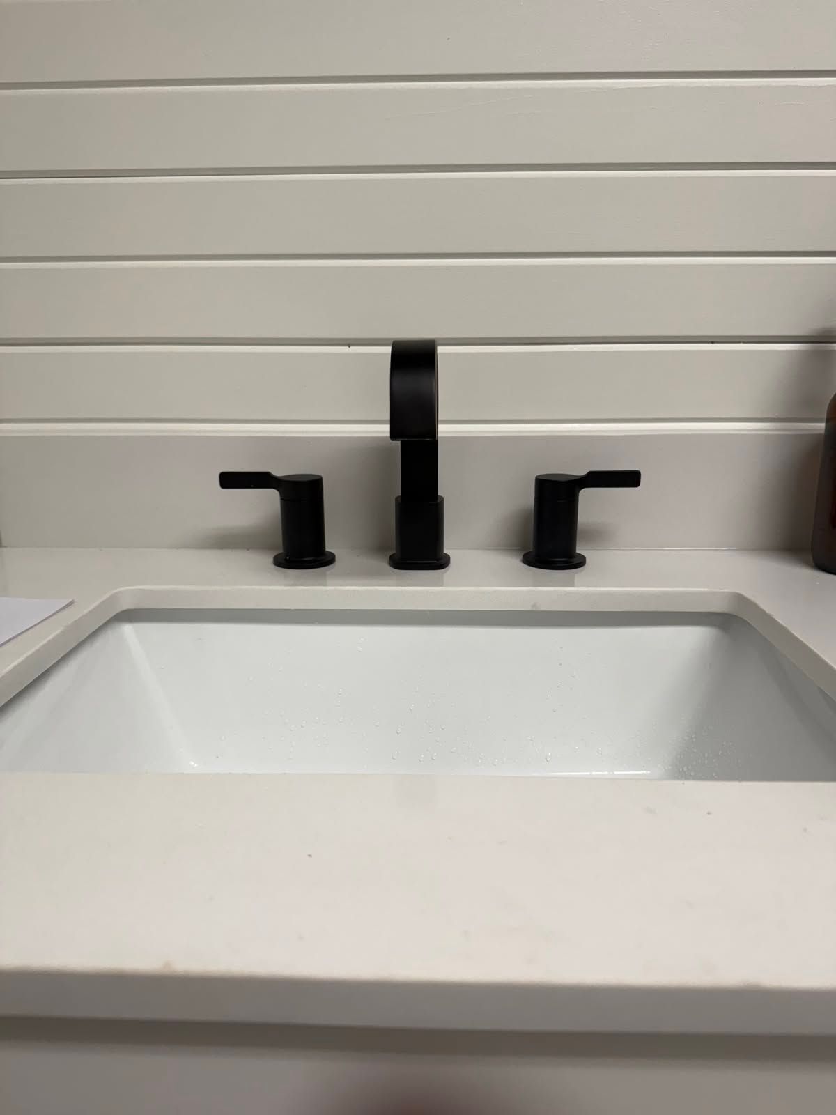 Modern bathroom sink with black faucet and handles against white tile wall