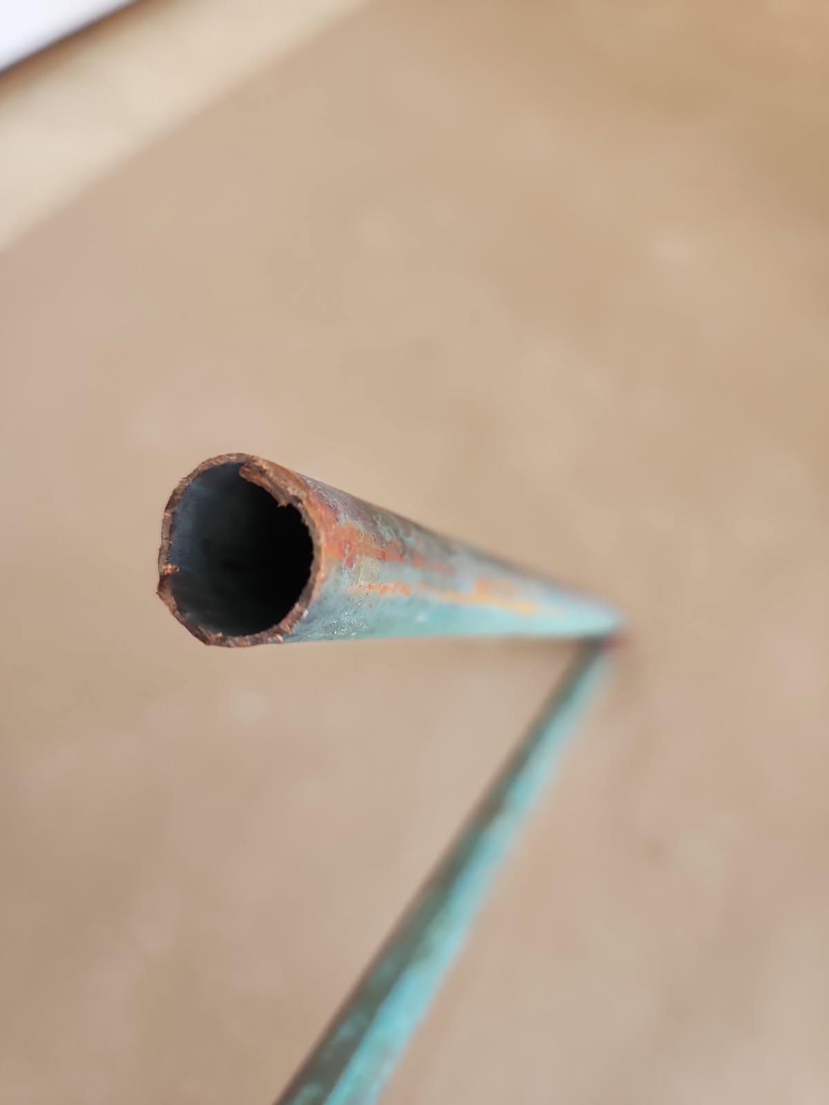 Close-up of a rusted blue metal pipe or bent tube against a beige background