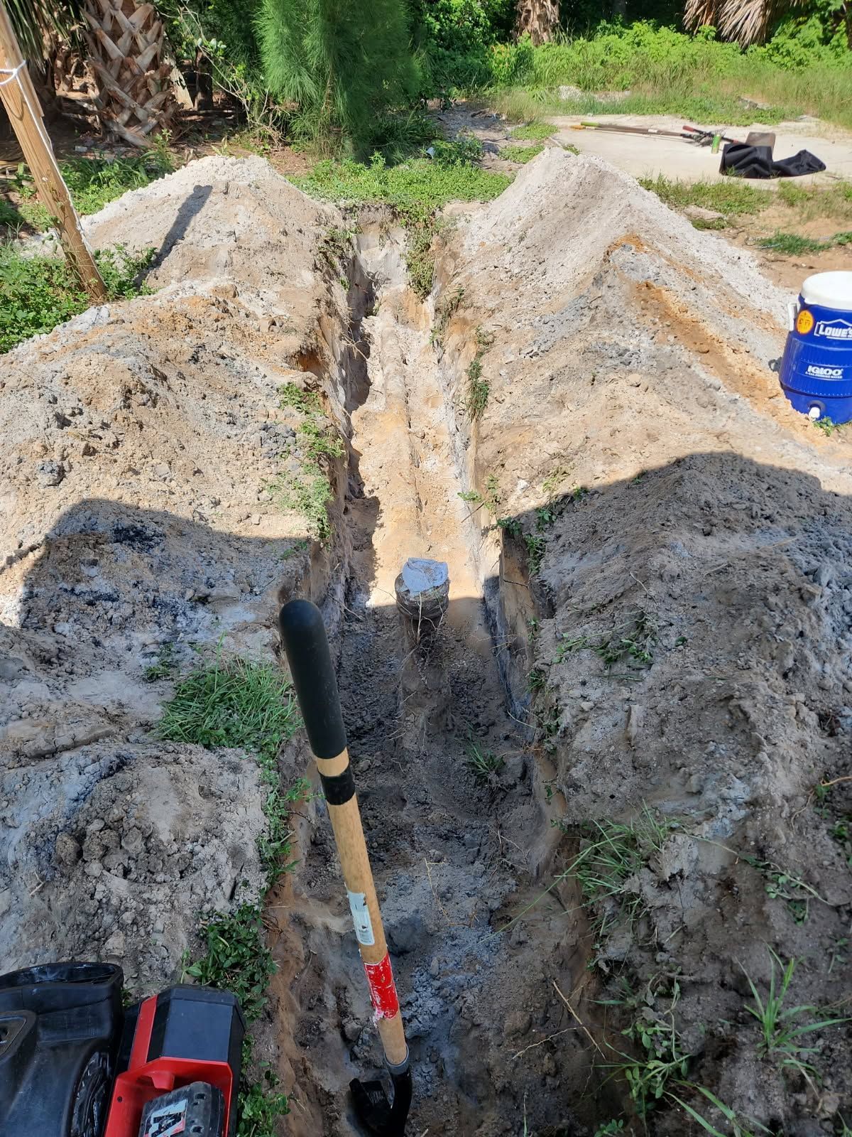 Freshly dug trench in a backyard with shovels and soil piles on both sides