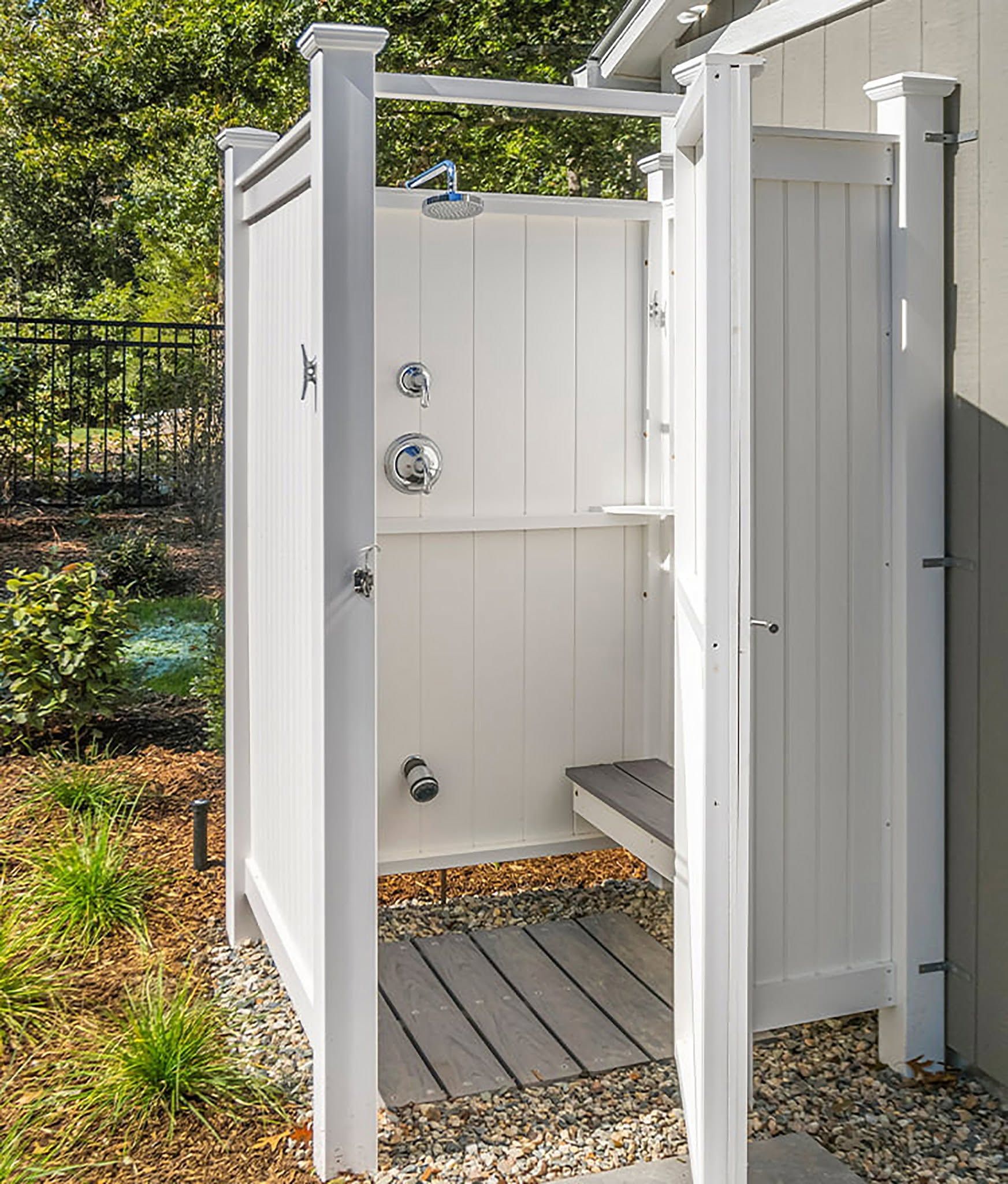Outdoor white accessible shower stall with open door, grab bars, and bench on a deck.