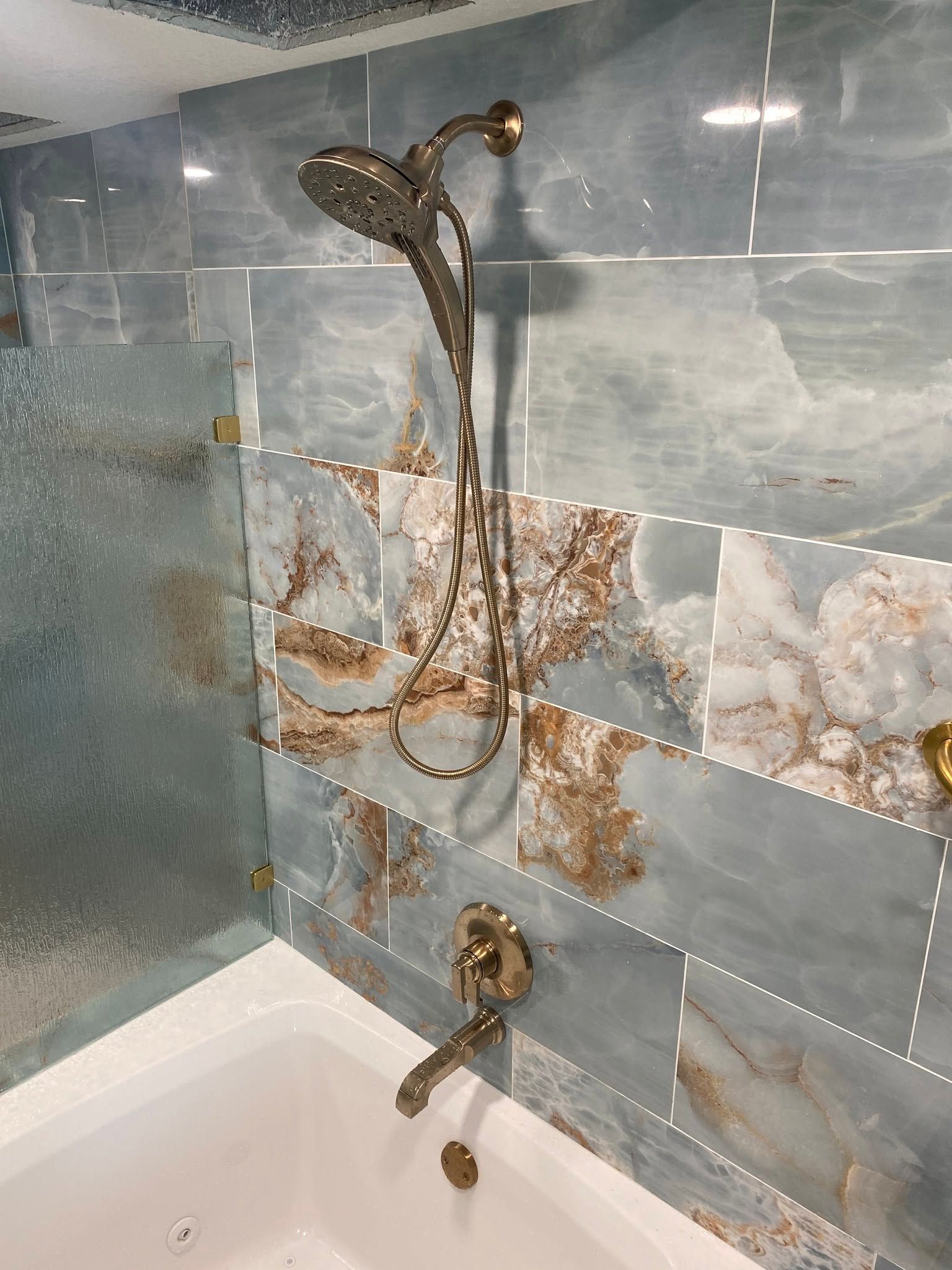 Bathroom wall with blue floral tiles and two exposed bronze shower fixtures with dangling cords