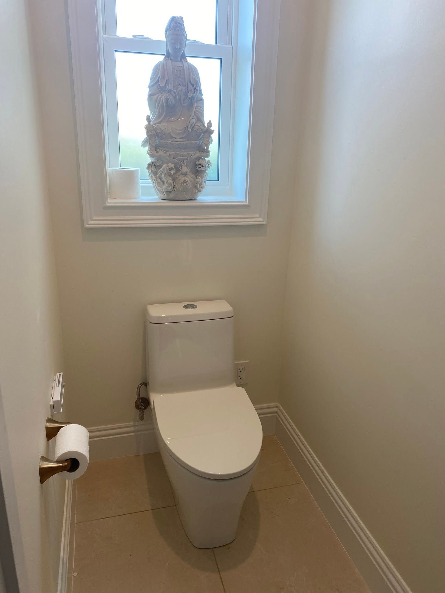 Small bathroom with a toilet beneath a frosted window and a toilet paper holder on the left wall.