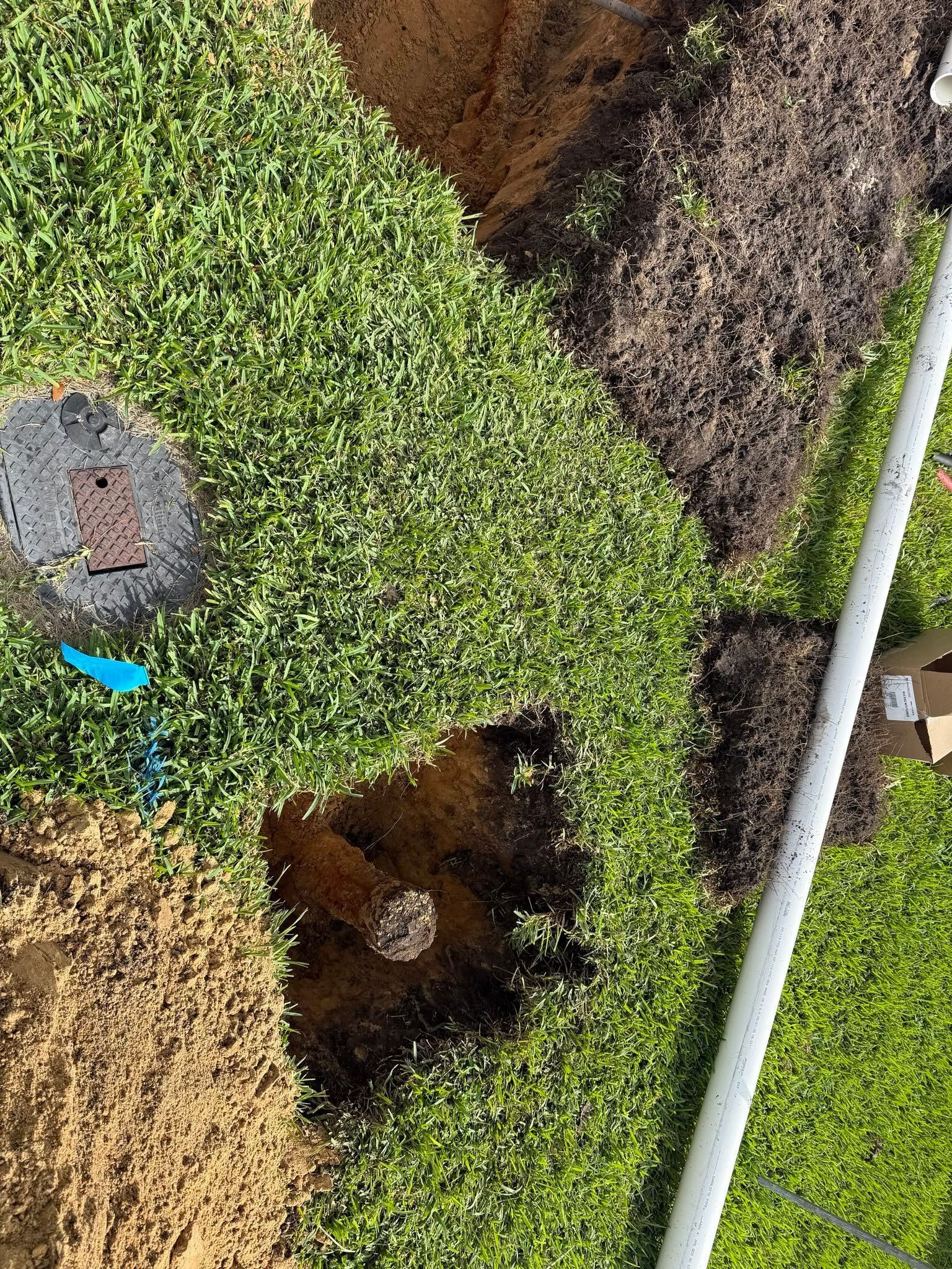 Small sinkhole in a grassy area beside a white pipe and a utility cover.