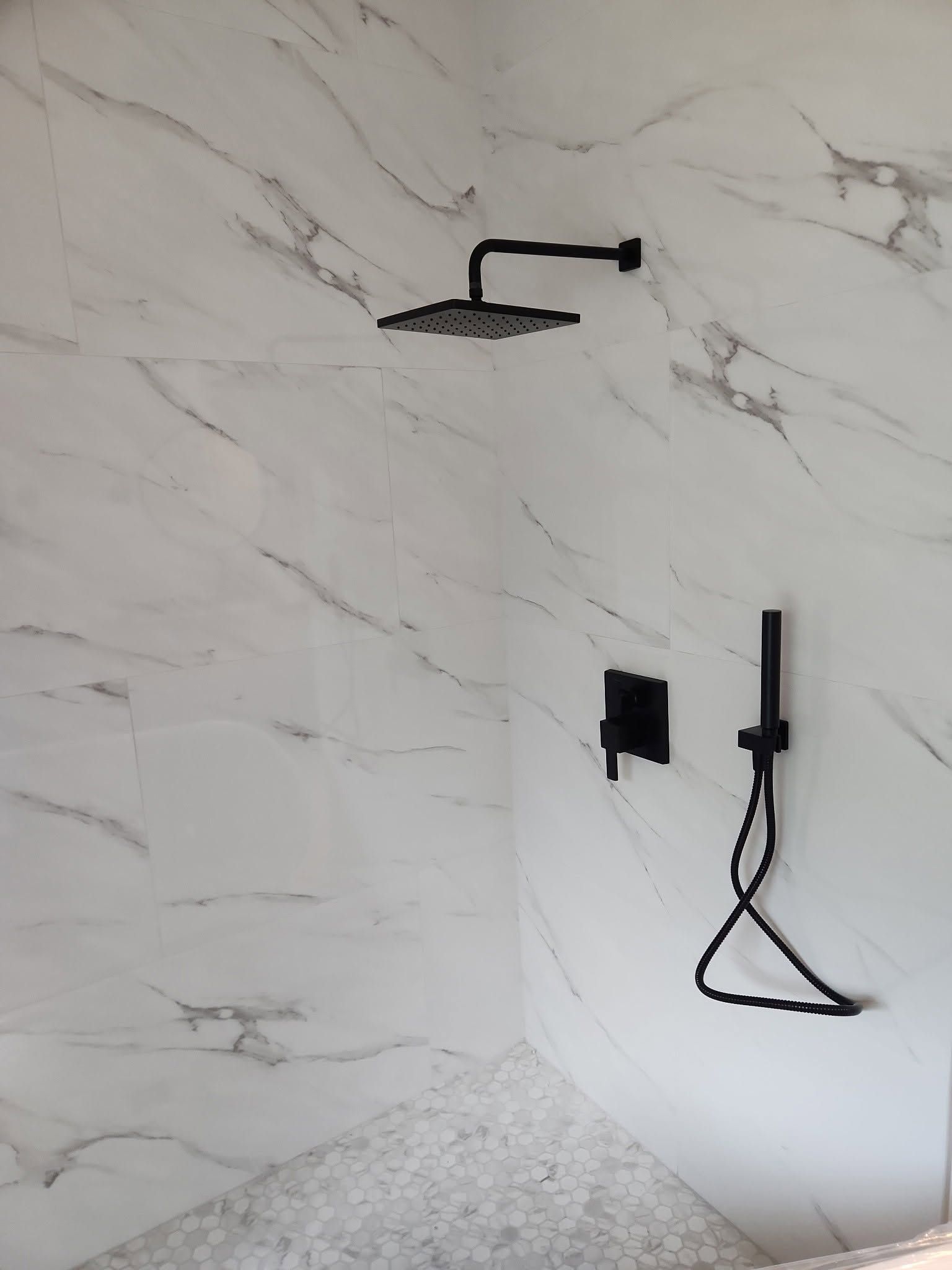 Modern shower with white marble tile, black shower fixtures, and a handheld sprayer on the wall.