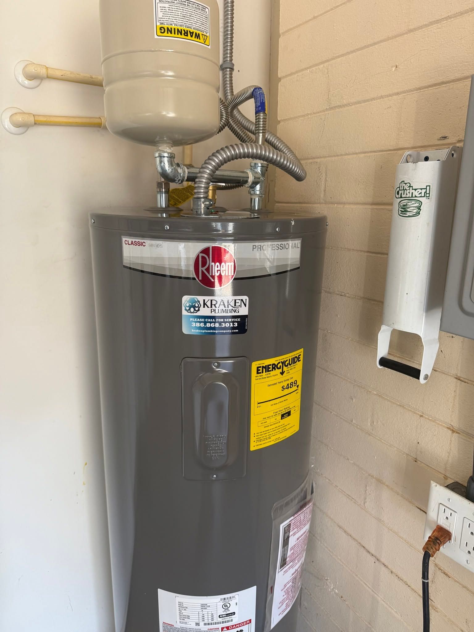 Water heater with pipes and valves in a utility room against beige tile walls.