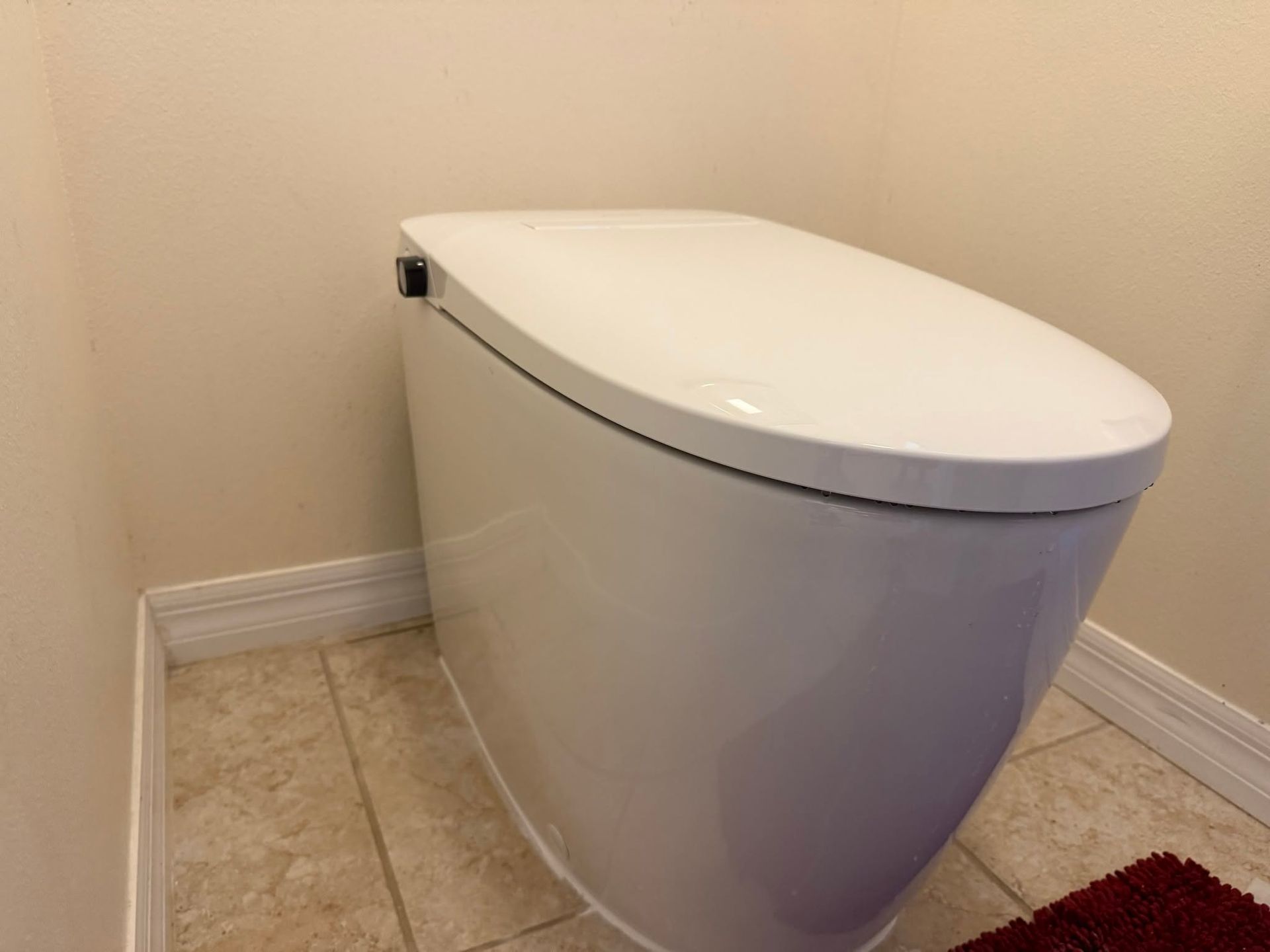 White modern toilet in a tiled bathroom corner against beige walls.