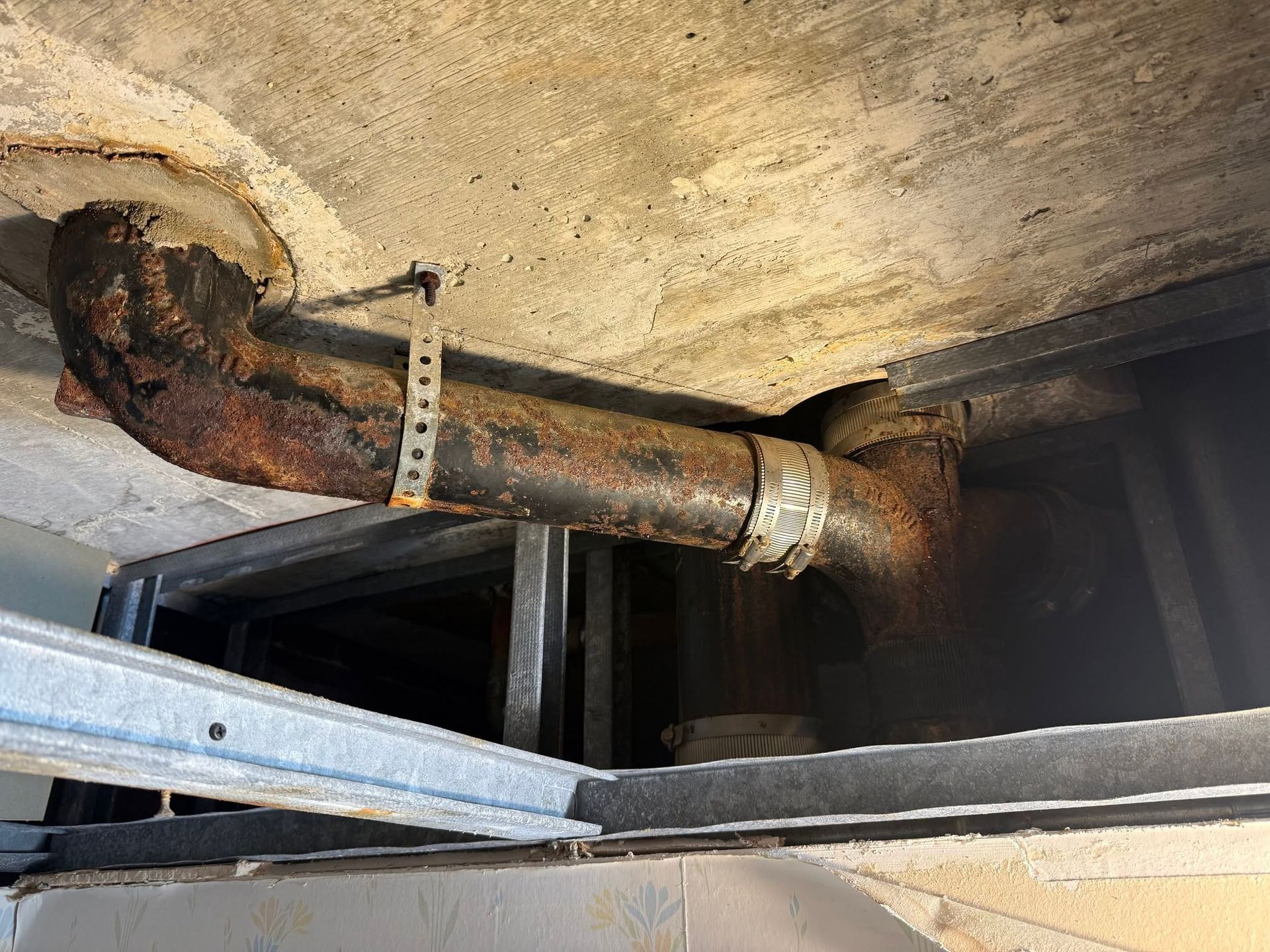Rusty corroded pipe running through a concrete ceiling with a metal support bracket nearby