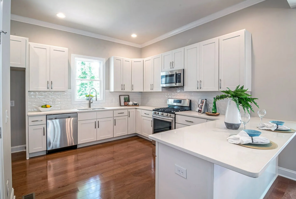 Bright modern white kitchen with large island, stainless appliances, and gray wood-look flooring