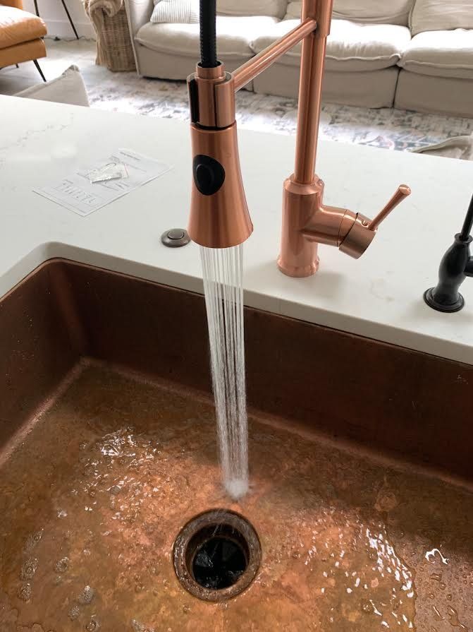 Copper kitchen faucet spraying water into a brown sink with a drain strainer