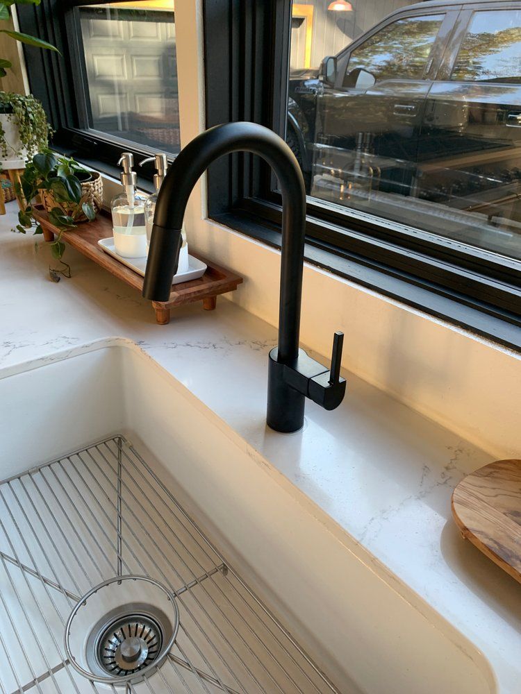 Modern kitchen sink with black faucet by a window, a drainboard, and a potted plant on the counter