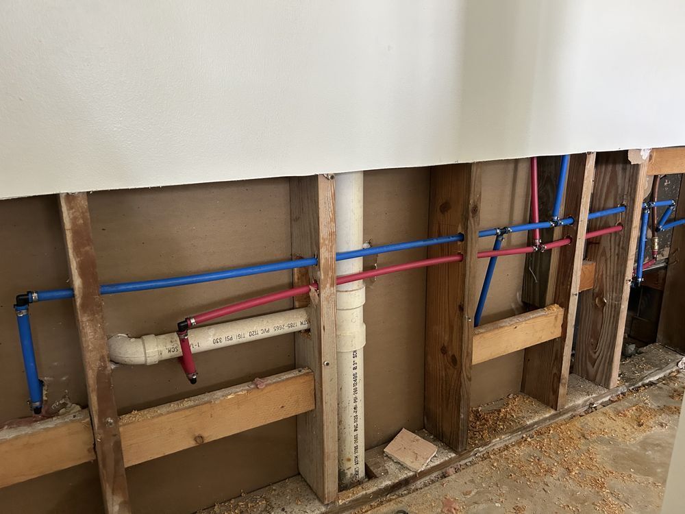 Exposed wall framing with blue and red plumbing pipes and a white drain pipe under renovation