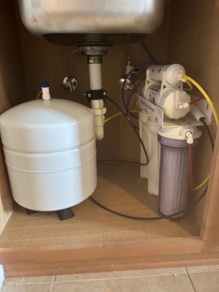 Under-sink water filtration system with white tank and filter housing in a wooden cabinet
