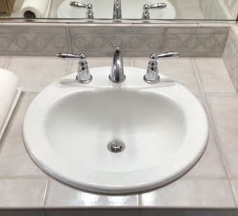 White bathroom sink with chrome faucet and handles on a tiled countertop