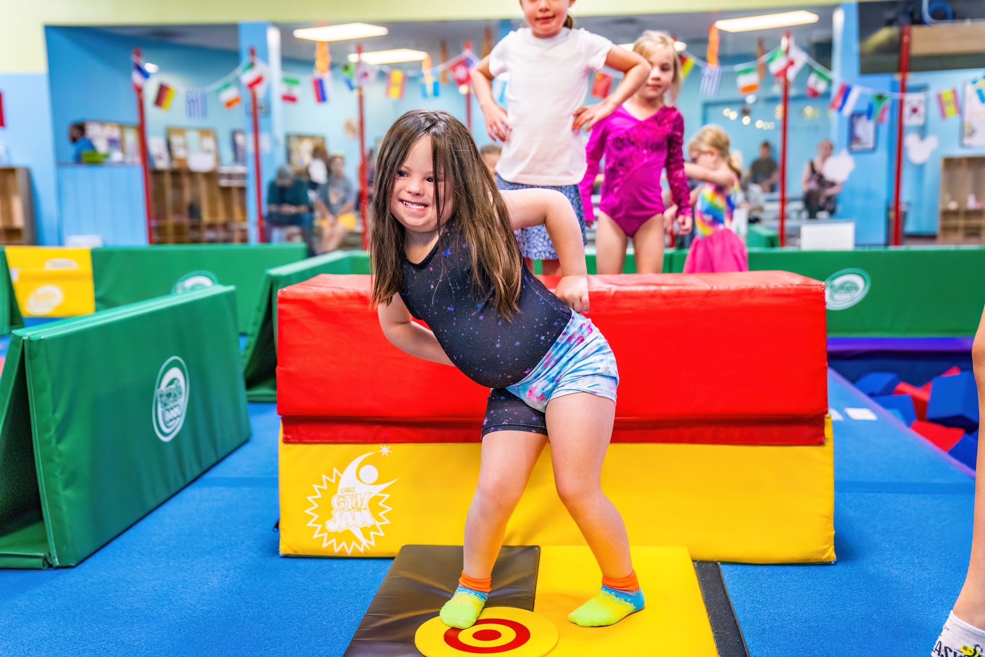 A little girl is standing on a mat in a gym.