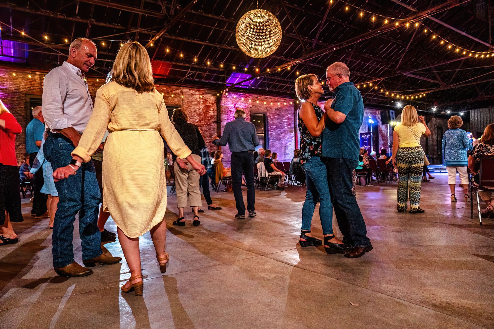 A group of people are dancing in a room with a disco ball hanging from the ceiling.
