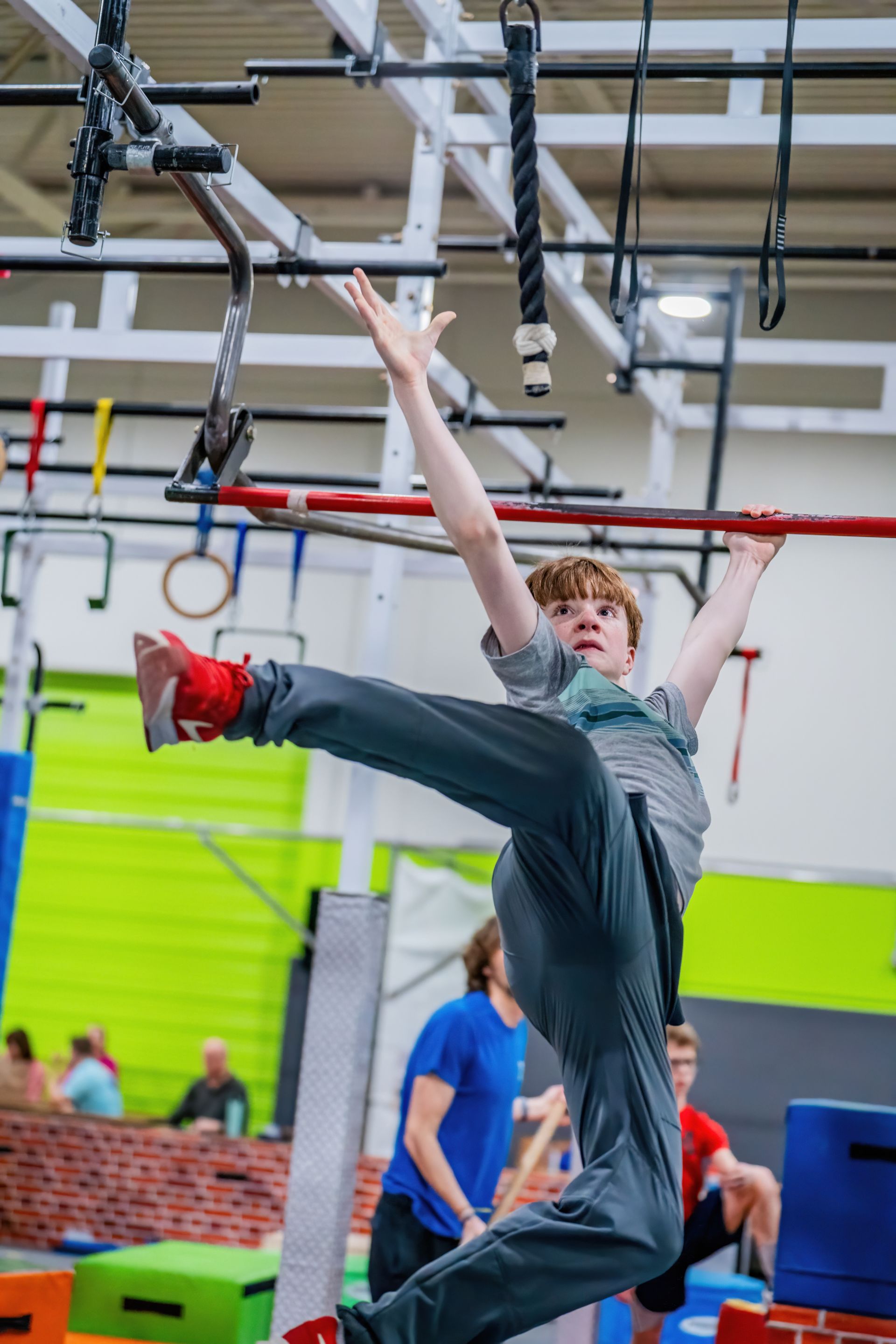 A young boy is jumping over a bar in a gym.