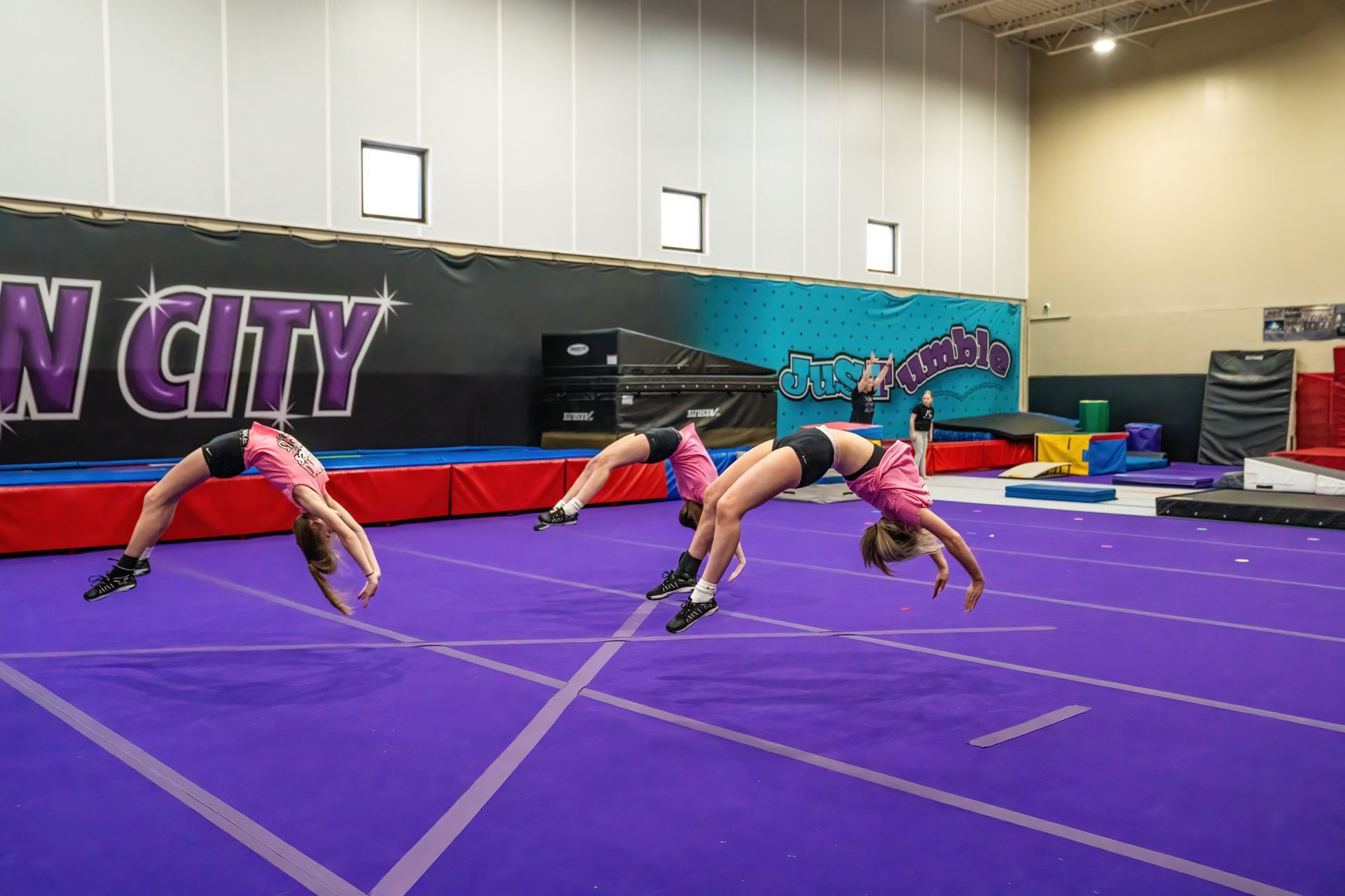 Three girls are doing a handstand on a purple mat in a gym.