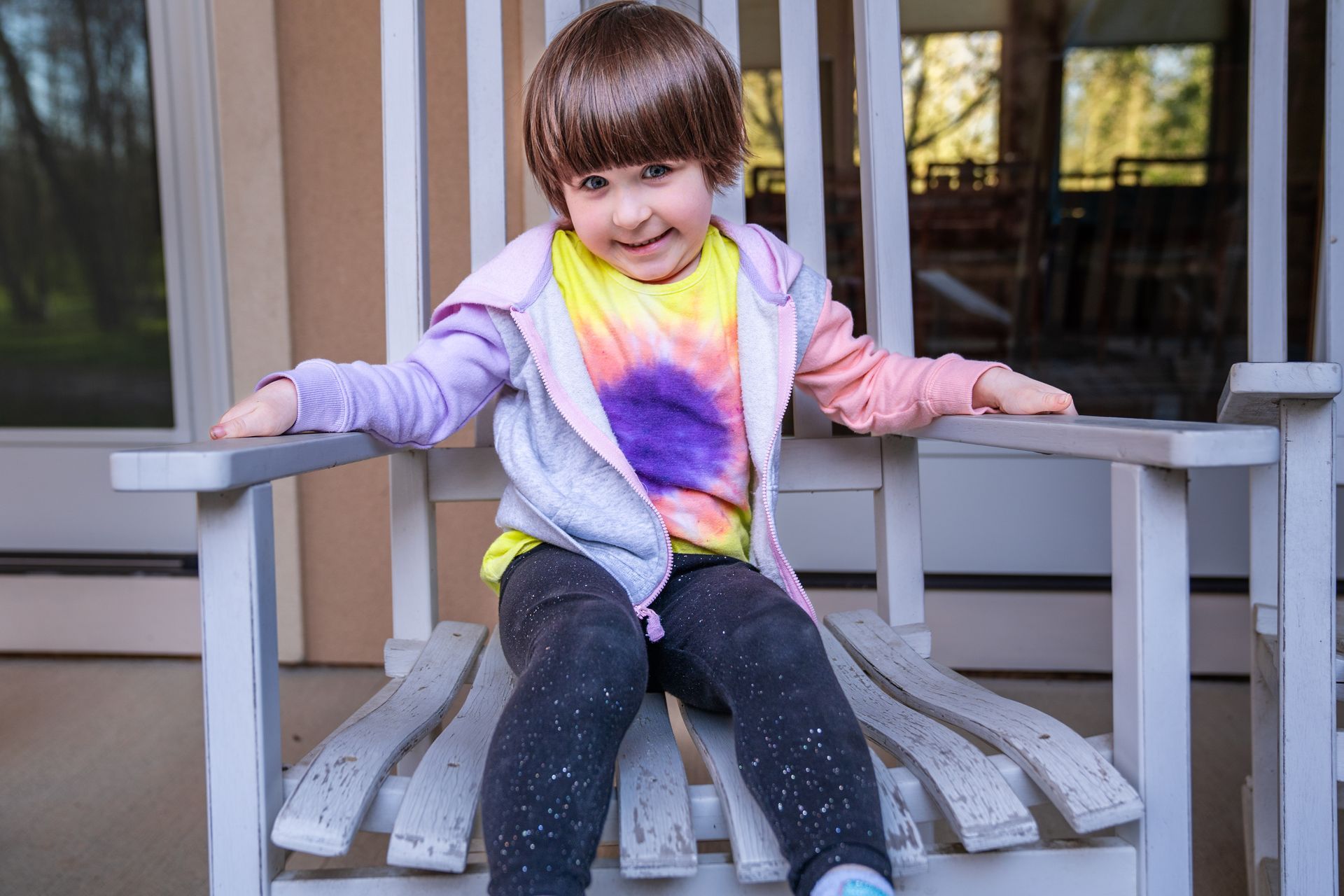 A little girl is sitting in a rocking chair on a porch.