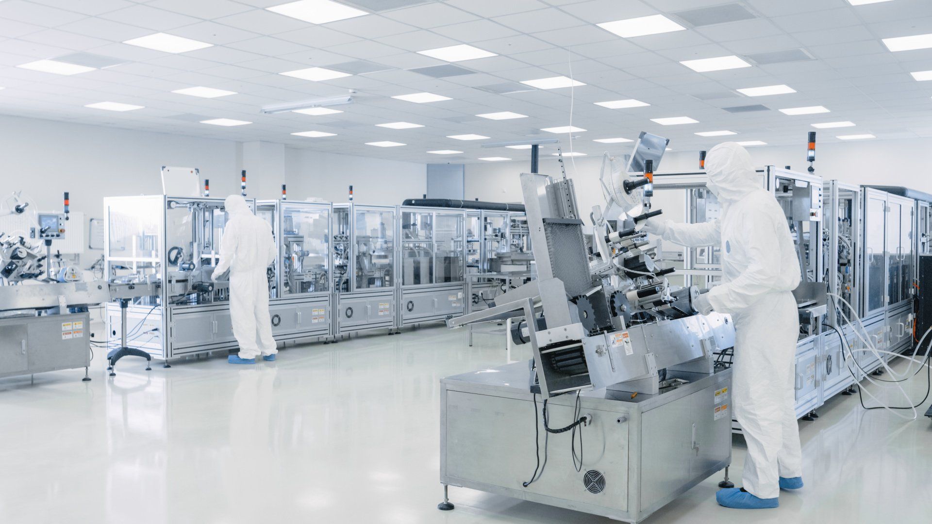 A man in a white suit is working on a machine in a clean room.