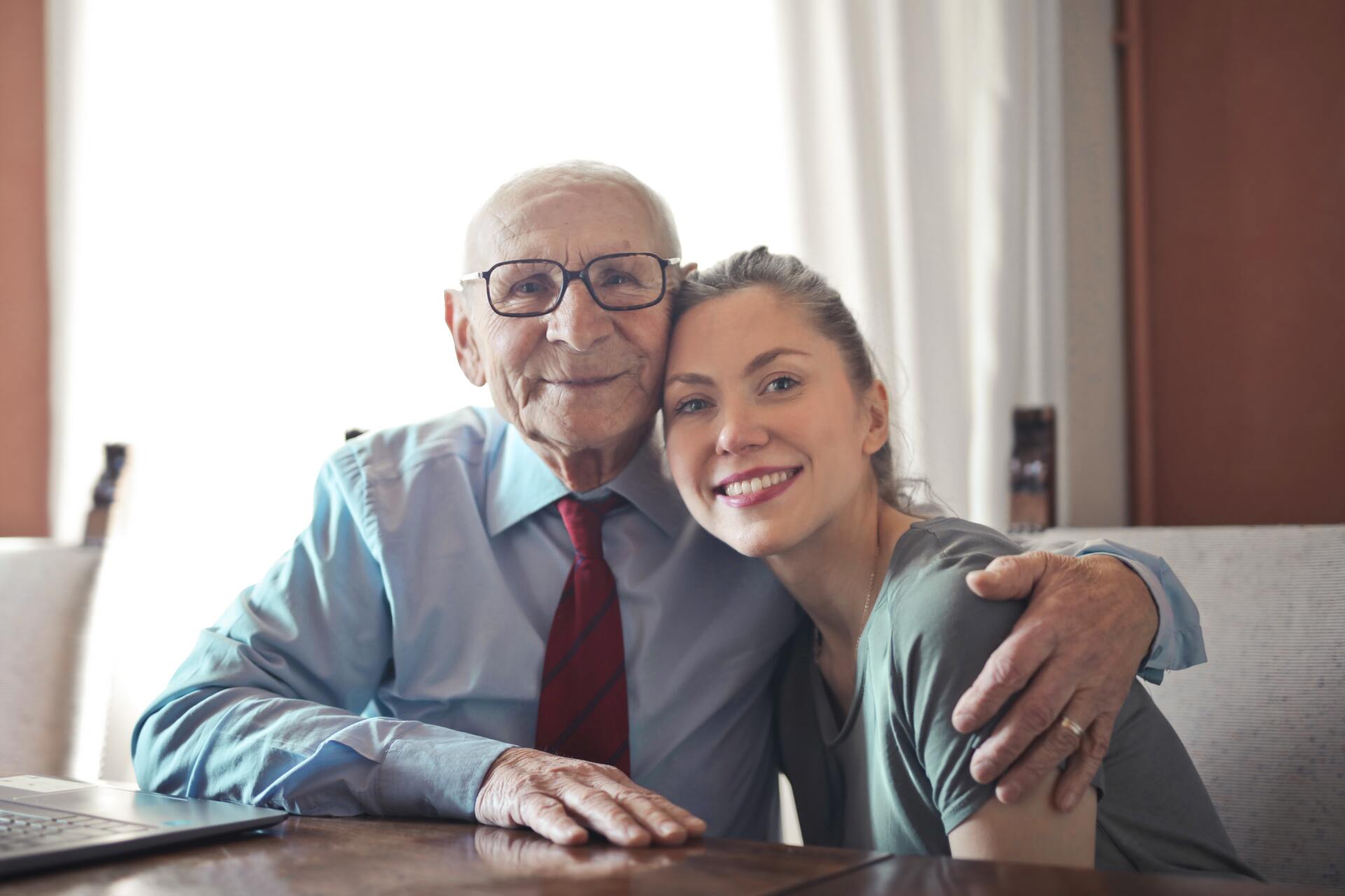 An older gentleman hugging his granddaughter, both are happy.